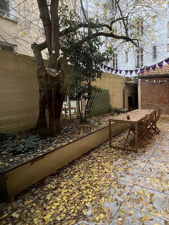 Cour intérieure arborée avec grande table en bois et guirlande